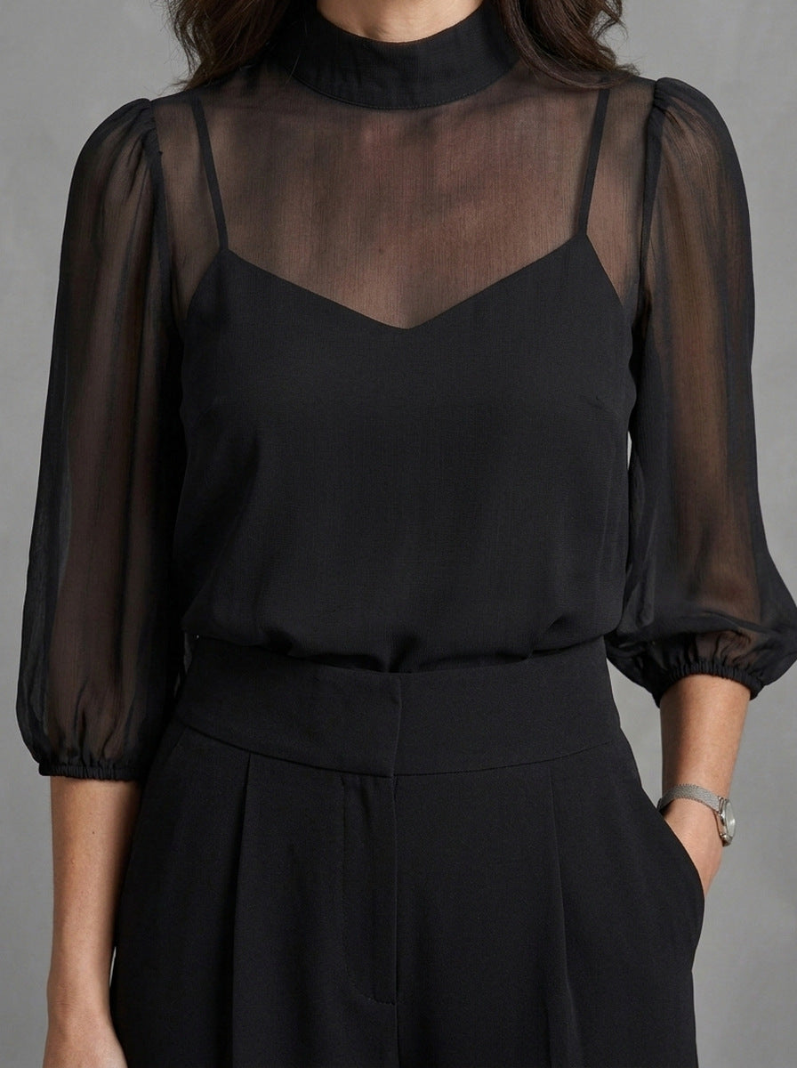 Dalia — completo nero, dettaglio della blusa trasparente a collo alto e delle maniche a palloncino